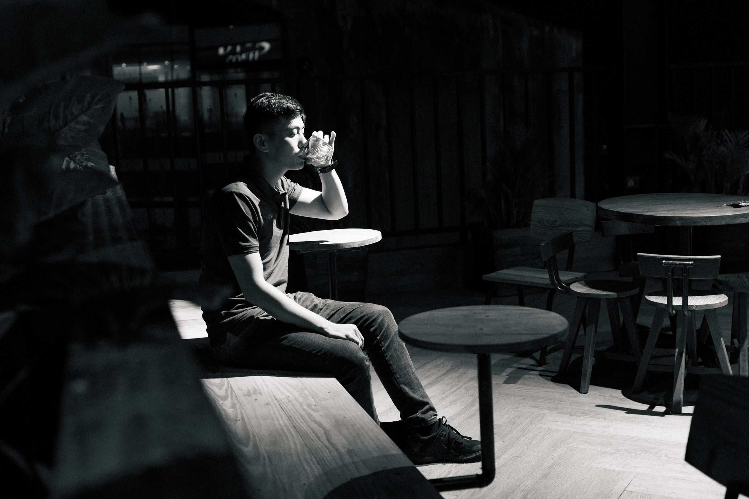Bărbat singur care bea noaptea într-un bar slab luminat, fotografie alb-negru