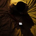 Bărbat întins în pat într-o cameră întunecată, cu fața luminată de ecranul telefonului