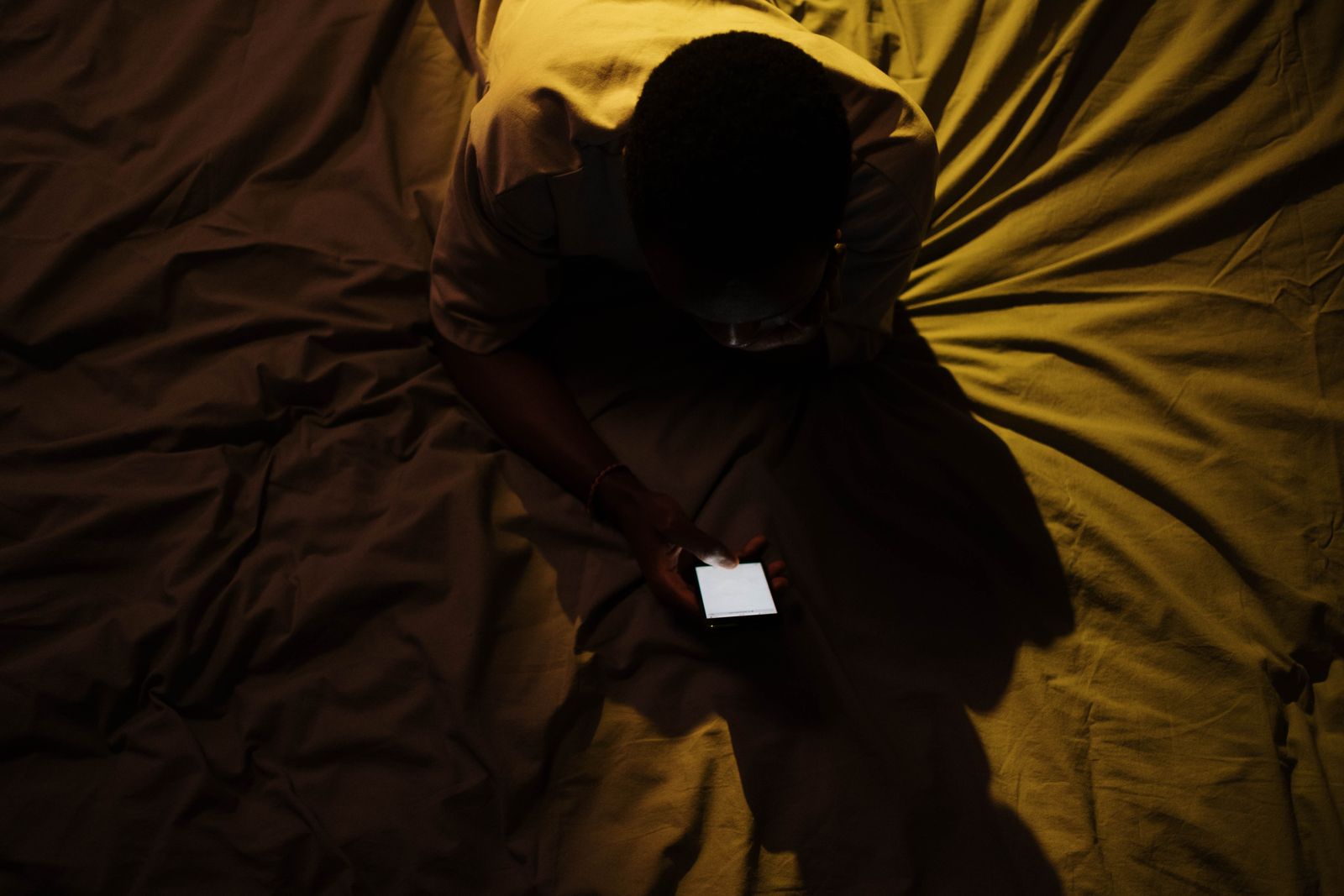 Bărbat întins în pat într-o cameră întunecată, cu fața luminată de ecranul telefonului