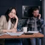 Un bărbat și o femeie la masă, citind împreună documente financiare, cu chipuri serioase