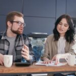 Un bărbat și o femeie discută la masa din casă, cu documente și căni de cafea în față