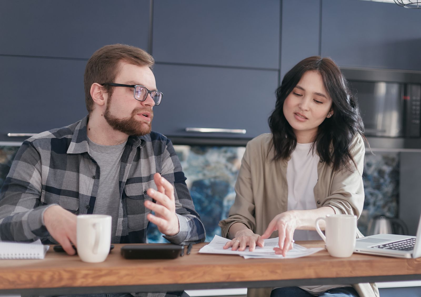 Un bărbat și o femeie discută la masa din casă, cu documente și căni de cafea în față