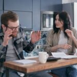 Bărbat îngrijorat discută cu soția la masa din bucătărie despre datorii și o posibilă refinanțare a creditelor