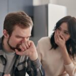 Bărbat îngrijorat stă lângă partenera lui, într-o discuție serioasă acasă