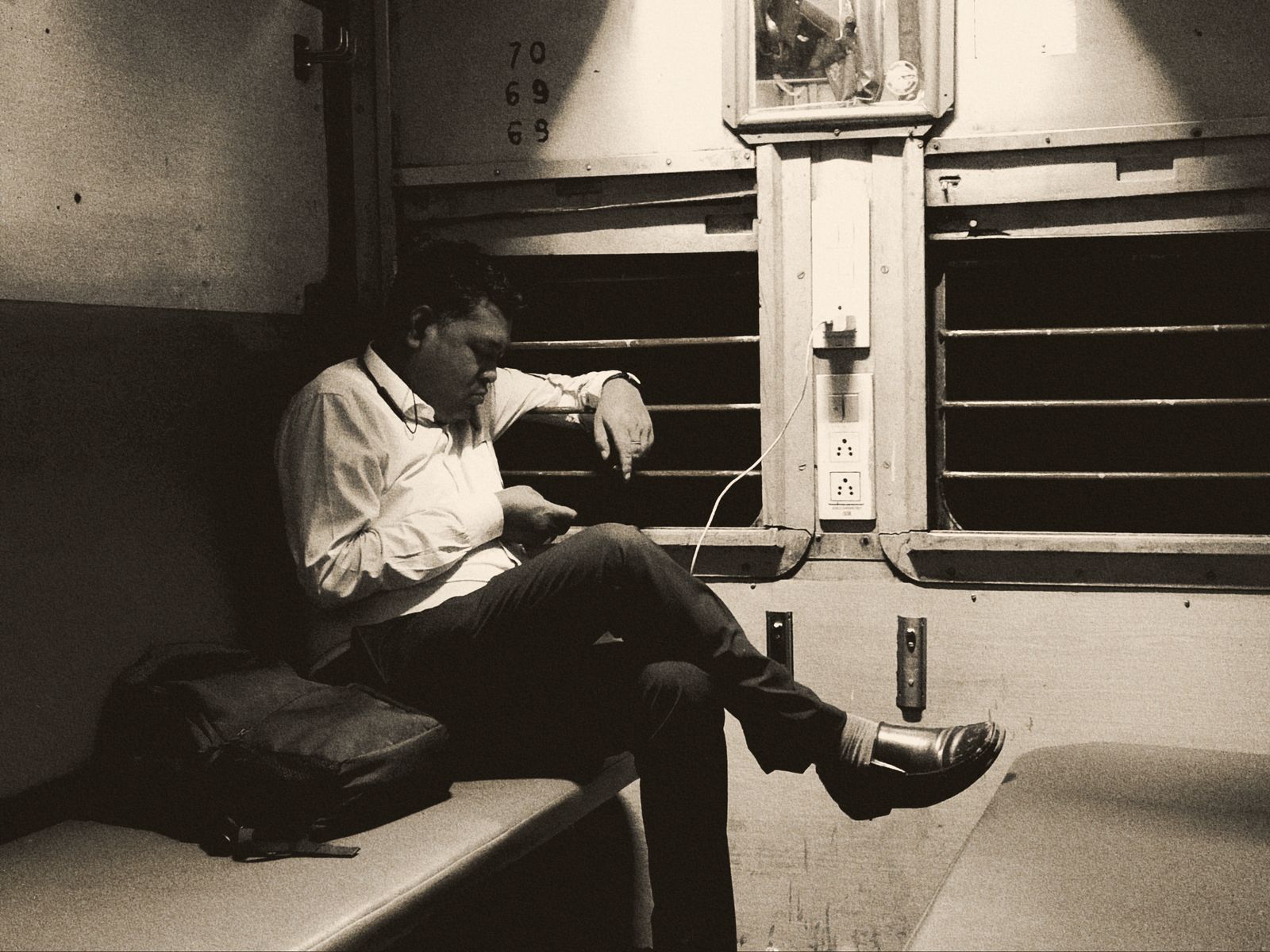 Bărbat singur într-un vagon de tren aproape gol, noaptea, cu privirea în telefon